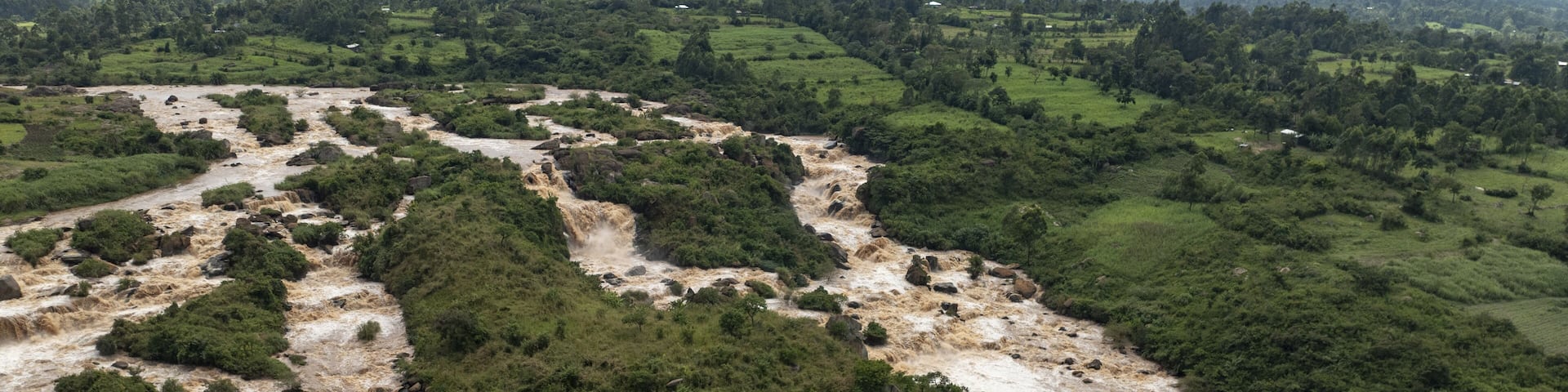 Aerial view of the Nzoia River's muddy waters carving through lush green landscapes, a symphony of earthy tones and verdant life, Webuye, Bungoma County, Kenya.
