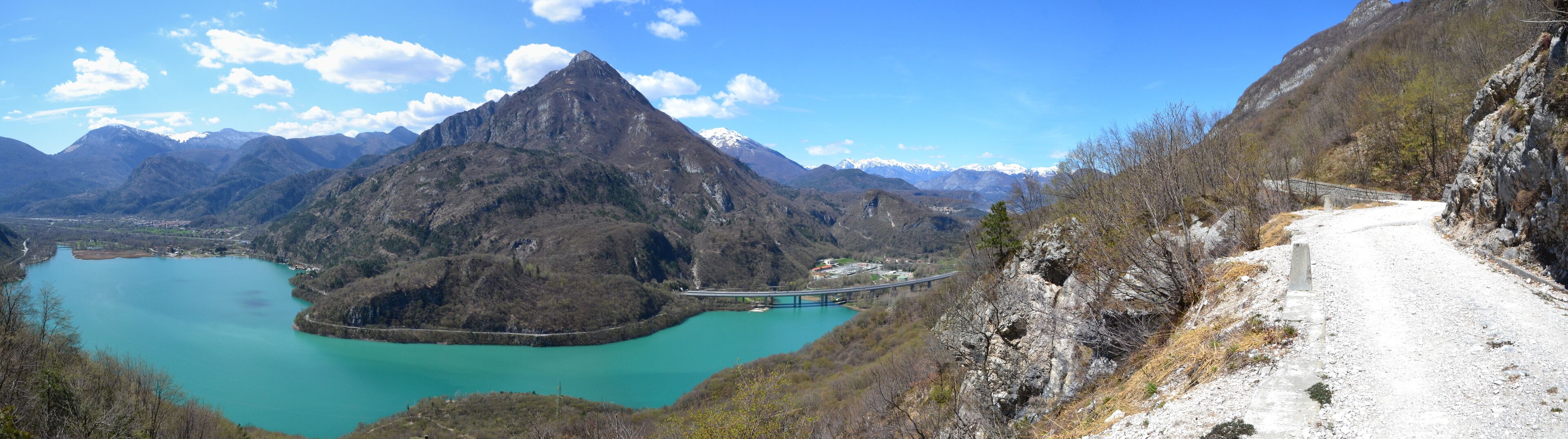 A mountain landscape with a turquoise lake, a bridge, and a road.