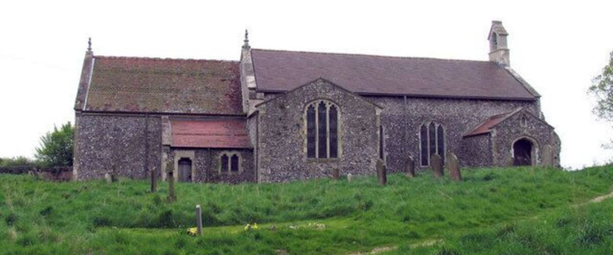 A stone church with a red roof on a grassy hill.