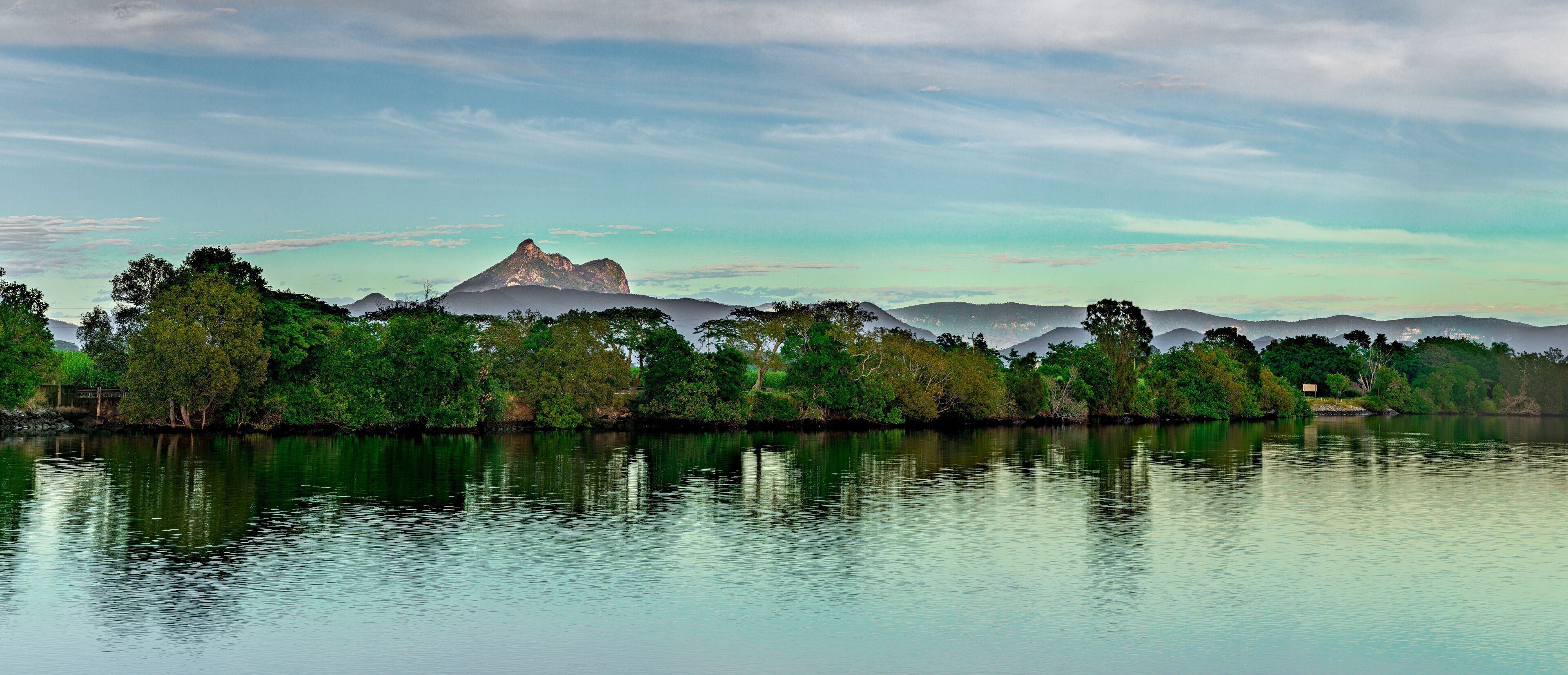 A calm lake with a mountain in the background and dense green trees along the shore.