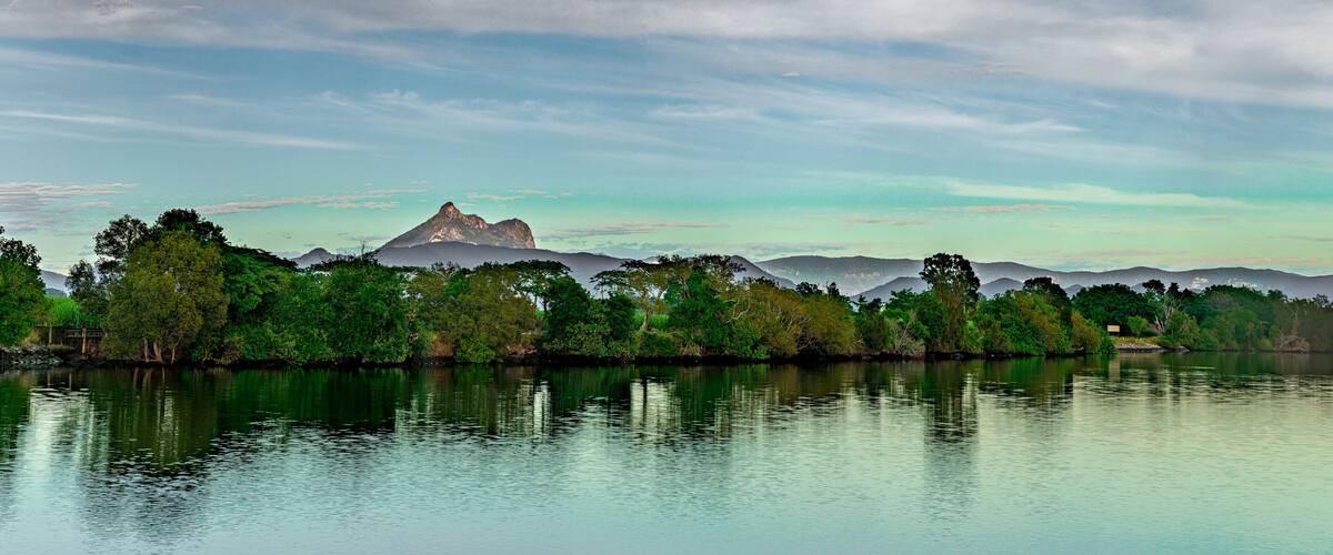 A calm lake with a mountain in the background and dense green trees along the shore.