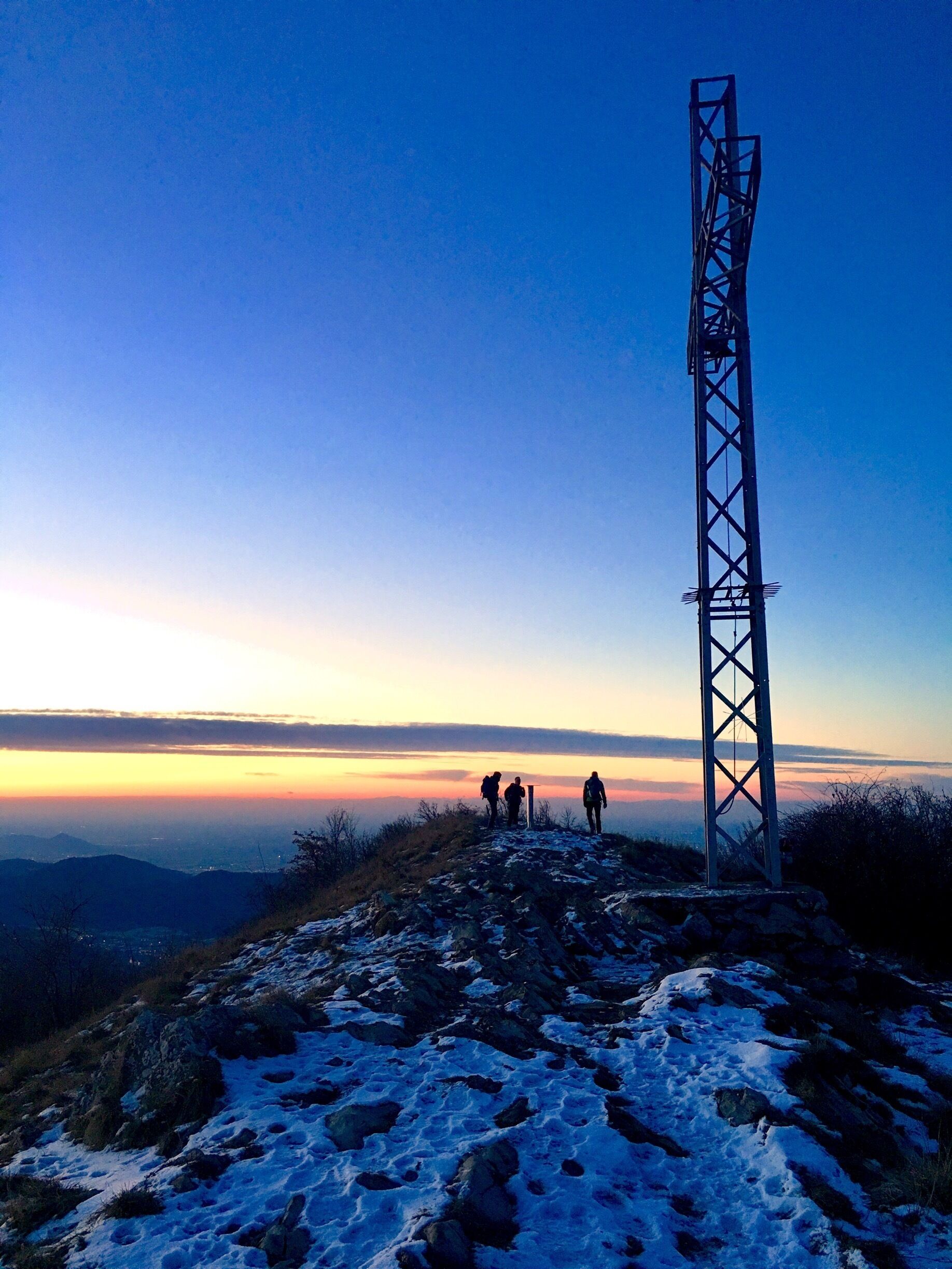 A metal tower on a snowy mountain ridge with hikers in the background.