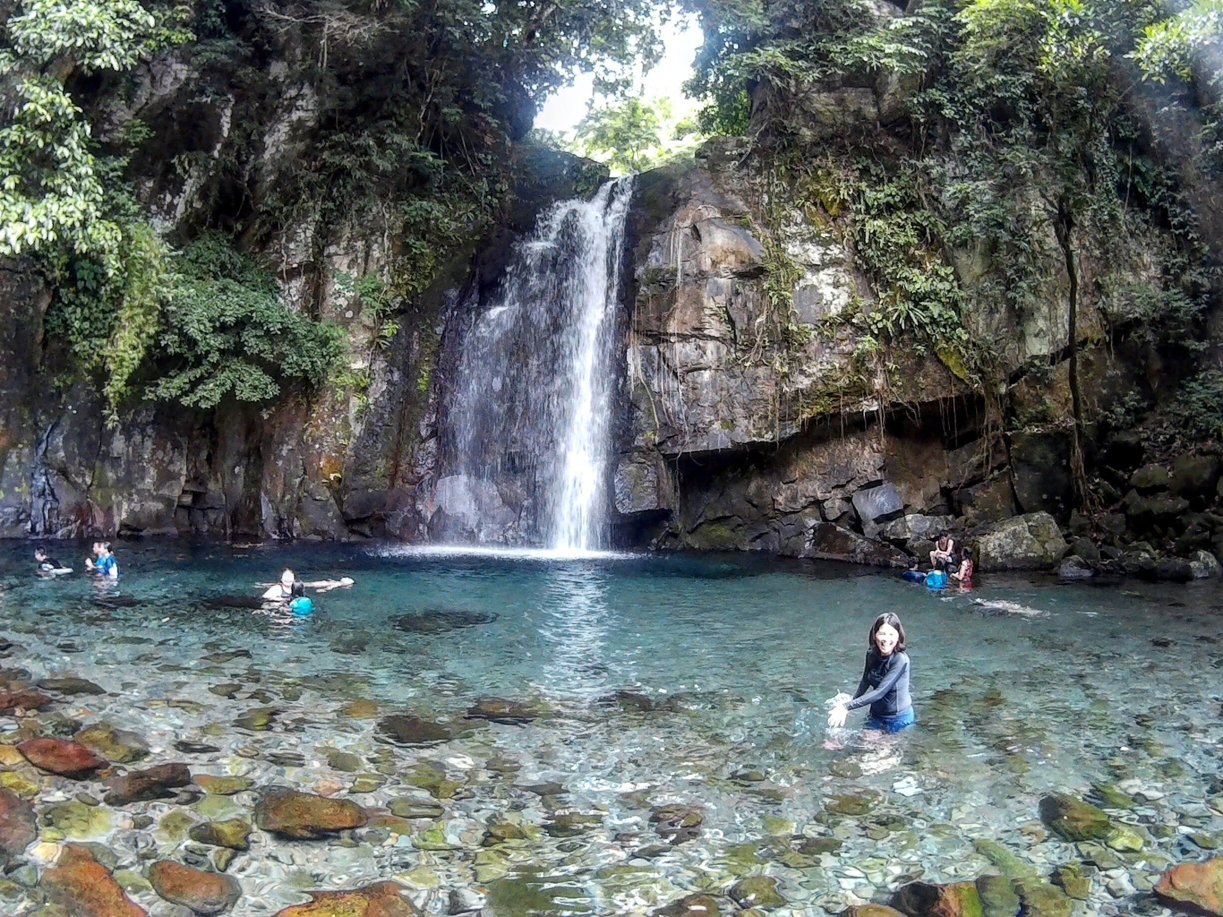 A waterfall cascading into a clear pool surrounded by rocky cliffs and lush greenery.