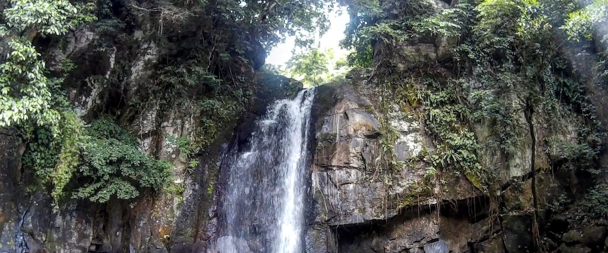 A waterfall cascading into a clear pool surrounded by rocky cliffs and lush greenery.