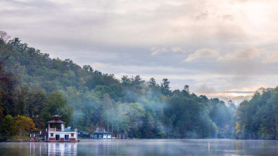 A lake with a row of houses and a forested hillside.