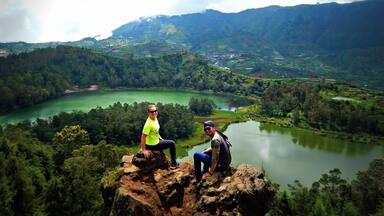 Duas pessoas sentadas em uma rocha com vista para um vale com campos em socalcos e um lago.