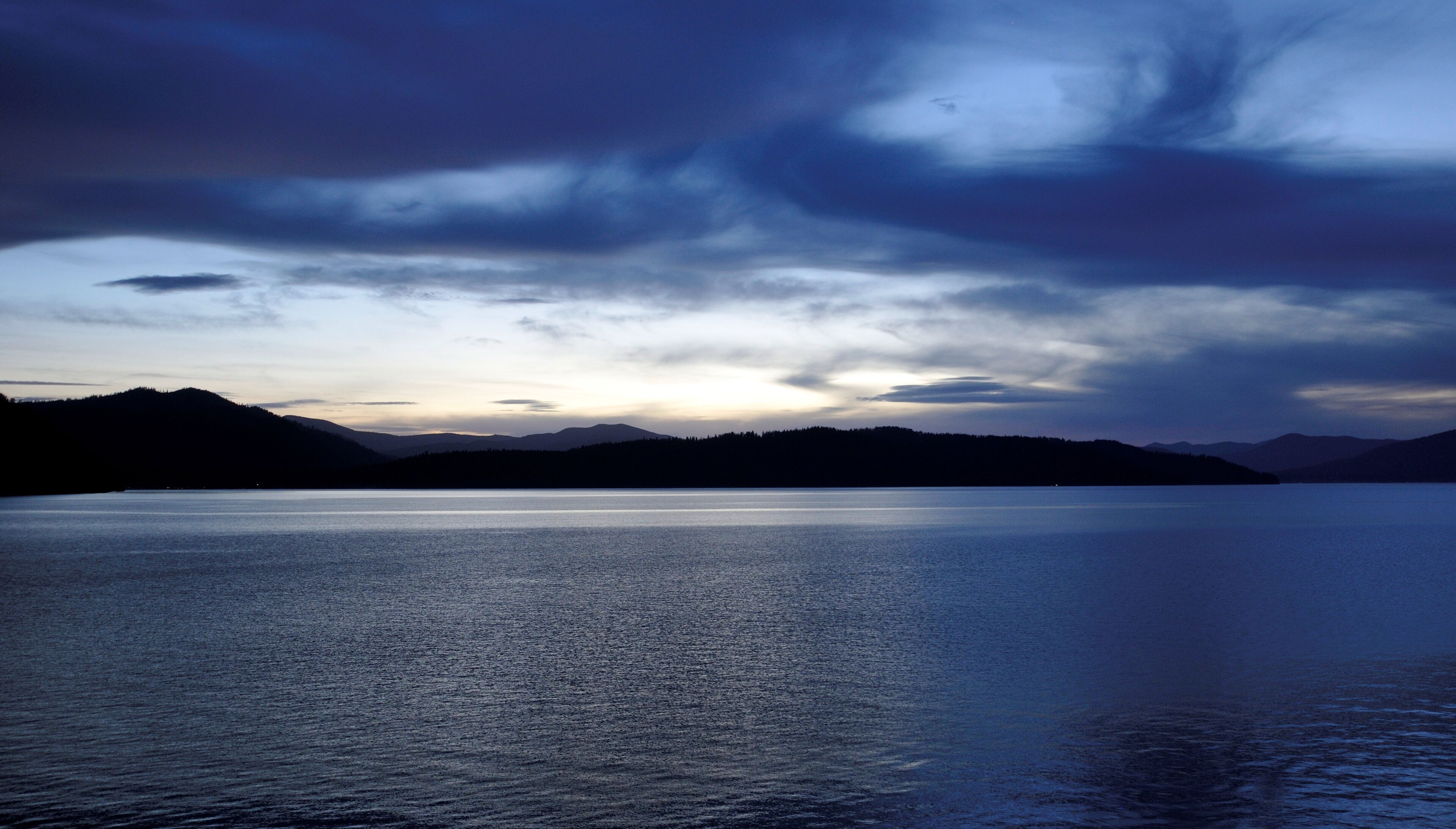 A calm lake at dusk with mountains in the background.