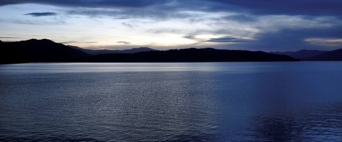 A calm lake at dusk with mountains in the background.