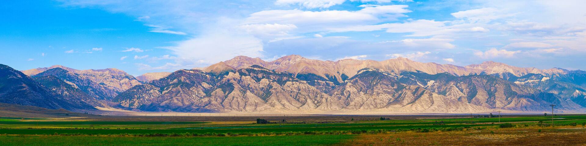A mountainous landscape with green fields in the foreground and snow-capped peaks in the background.