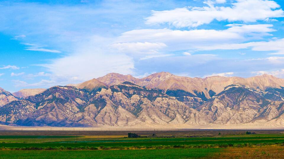 A mountainous landscape with green fields in the foreground and snow-capped peaks in the background.
