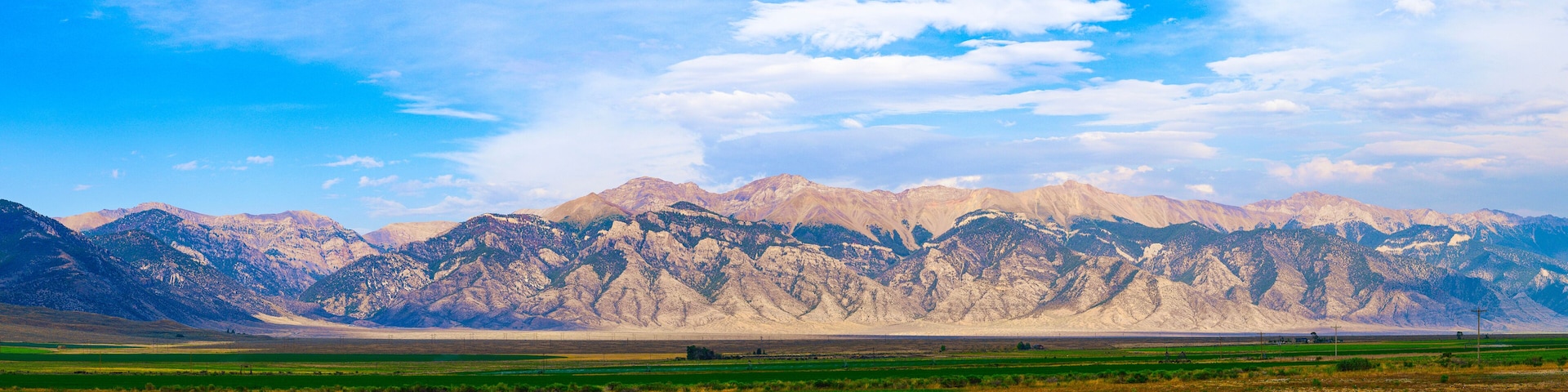 Paisagem montanhosa com campos verdejantes em primeiro plano e picos nevados ao fundo.