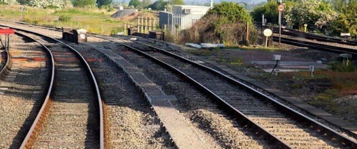 Railway tracks with a signal post and a bridge in the background.