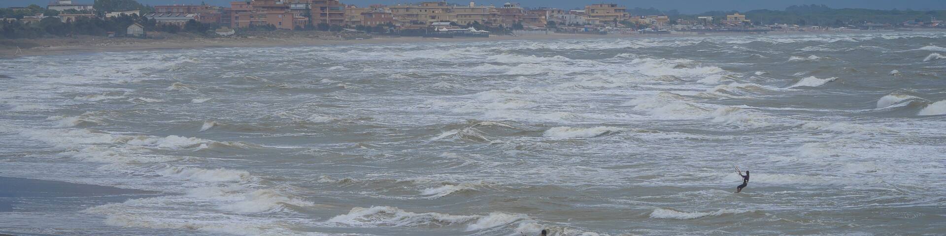 Two unrecognizable kiters in the stormy sea at Marina di San Nicola beach in Italy