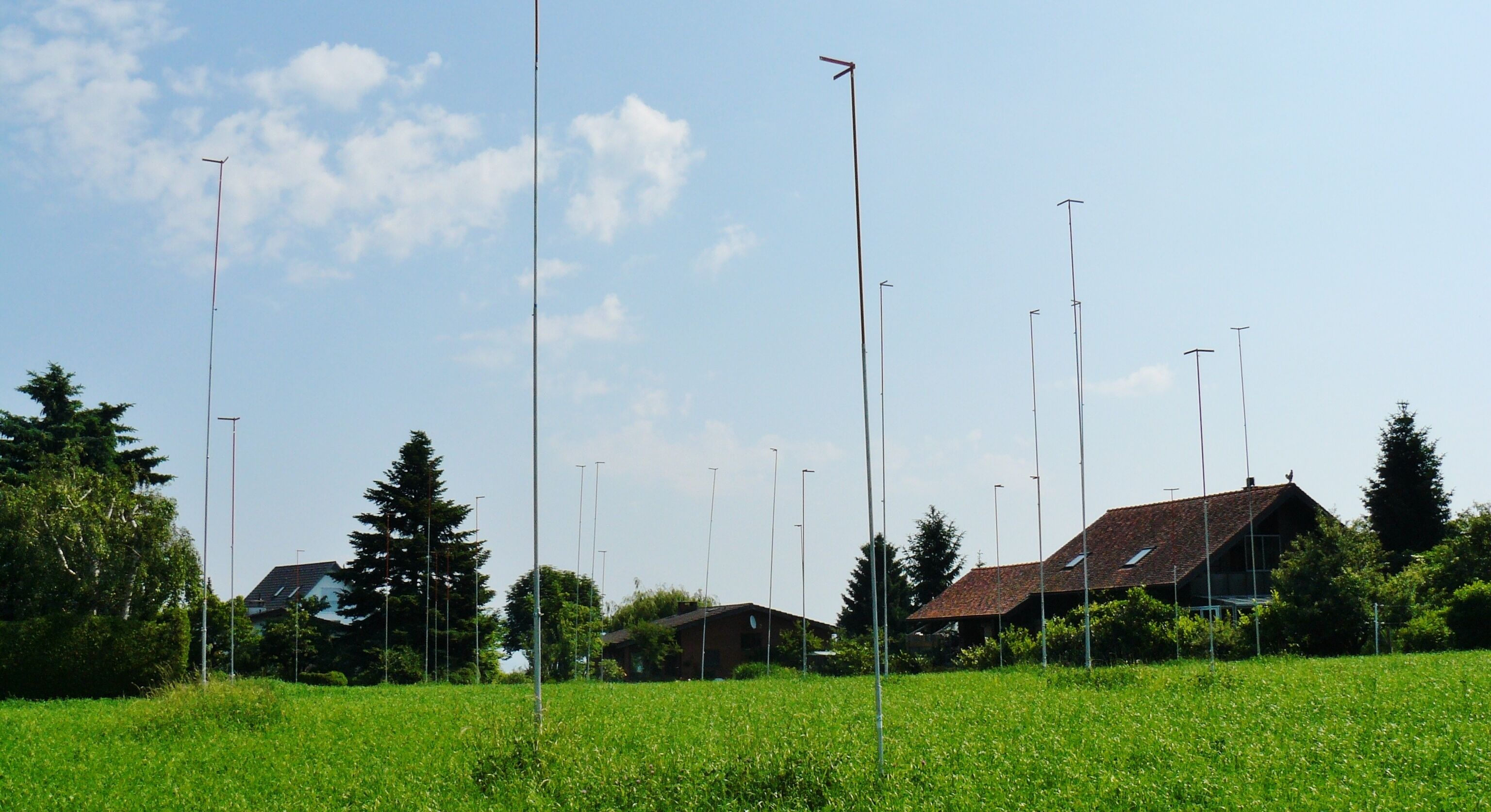 A field with tall poles, a house with a red roof, and a clear blue sky.