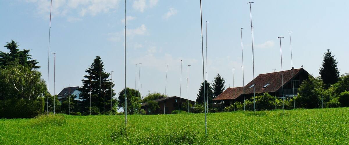 A field with tall poles, a house with a red roof, and a clear blue sky.