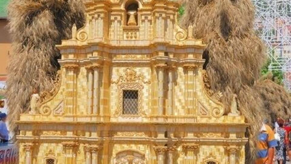 A golden replica of a church with two large trees on its roof, a sign reading "Gli amici del tesine presentano la chiesa madre," and a Ferris wheel in the background.