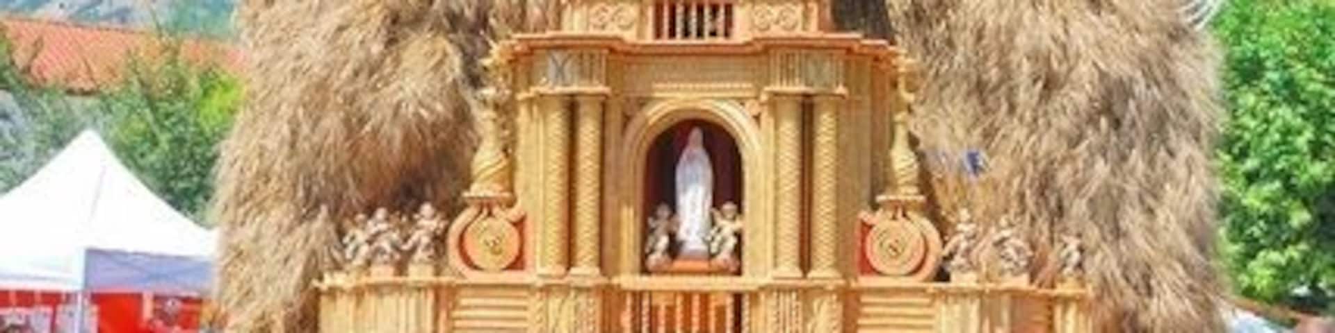 A wooden church model with a bell tower, surrounded by people and a Ferris wheel in the background.