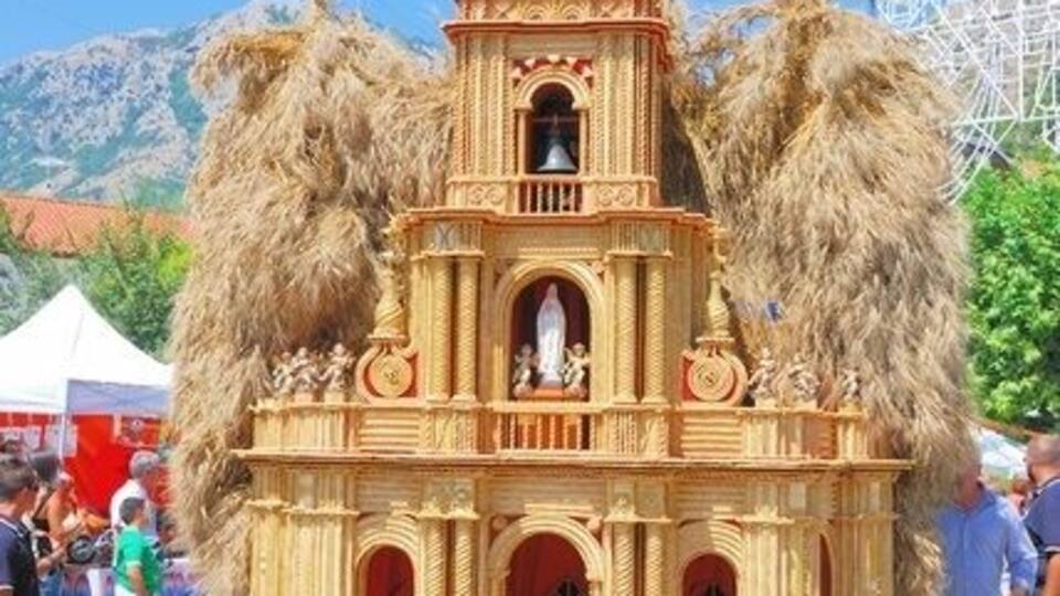 A wooden church model with a bell tower, surrounded by people and a Ferris wheel in the background.