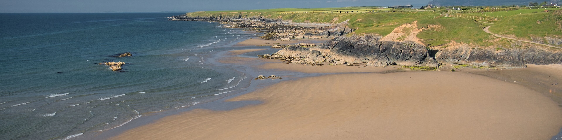 A coastal landscape with a sandy beach, rocky outcrops, and a distant mountain range.