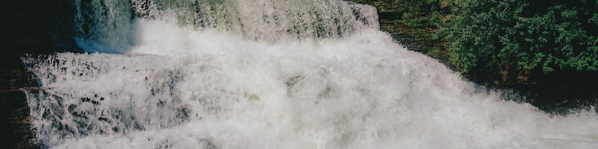 Una cascada se precipita sobre un saliente rocoso rodeado de exuberante follaje verde.