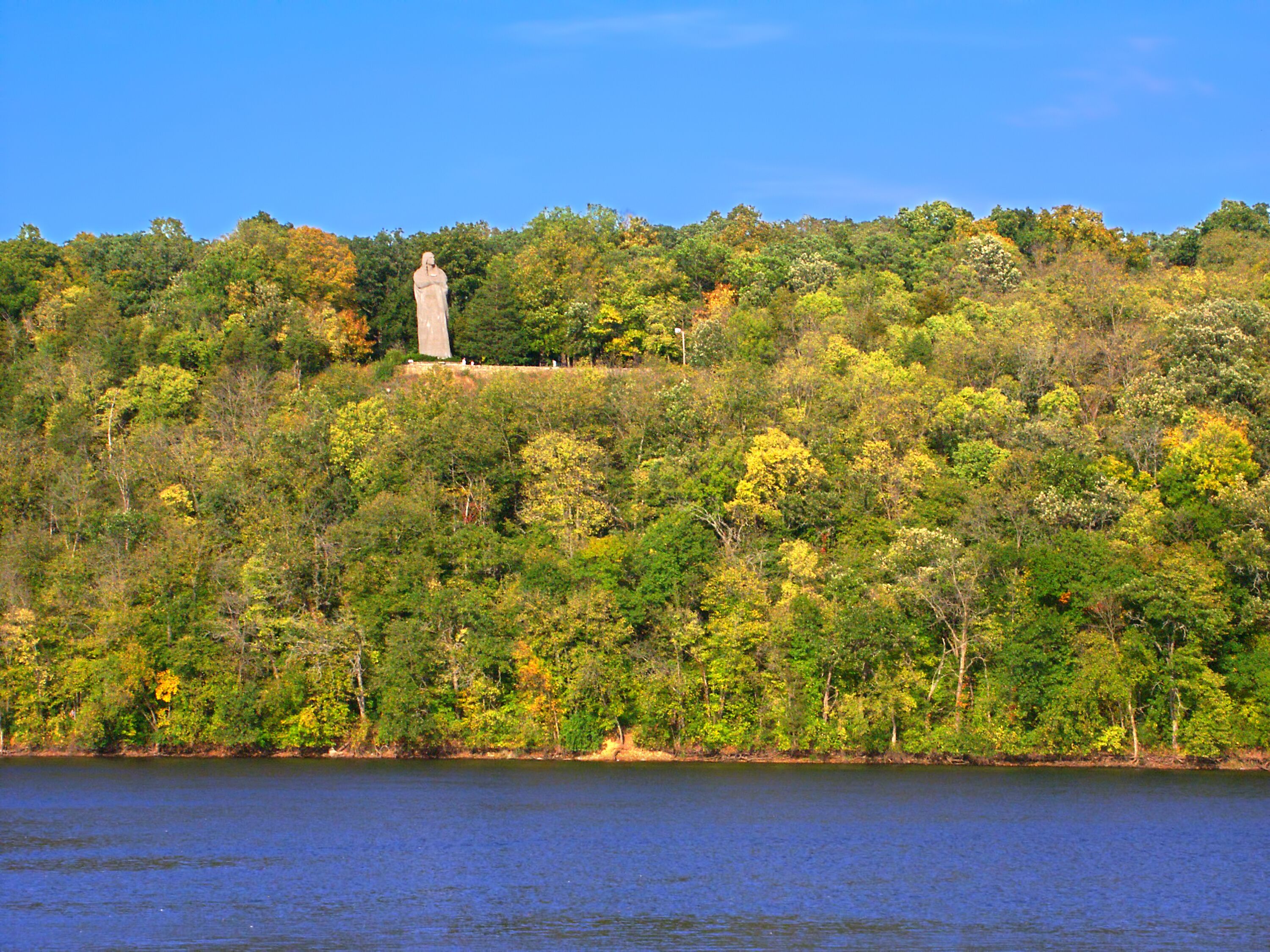 A statue on a hill with a lake in the foreground.