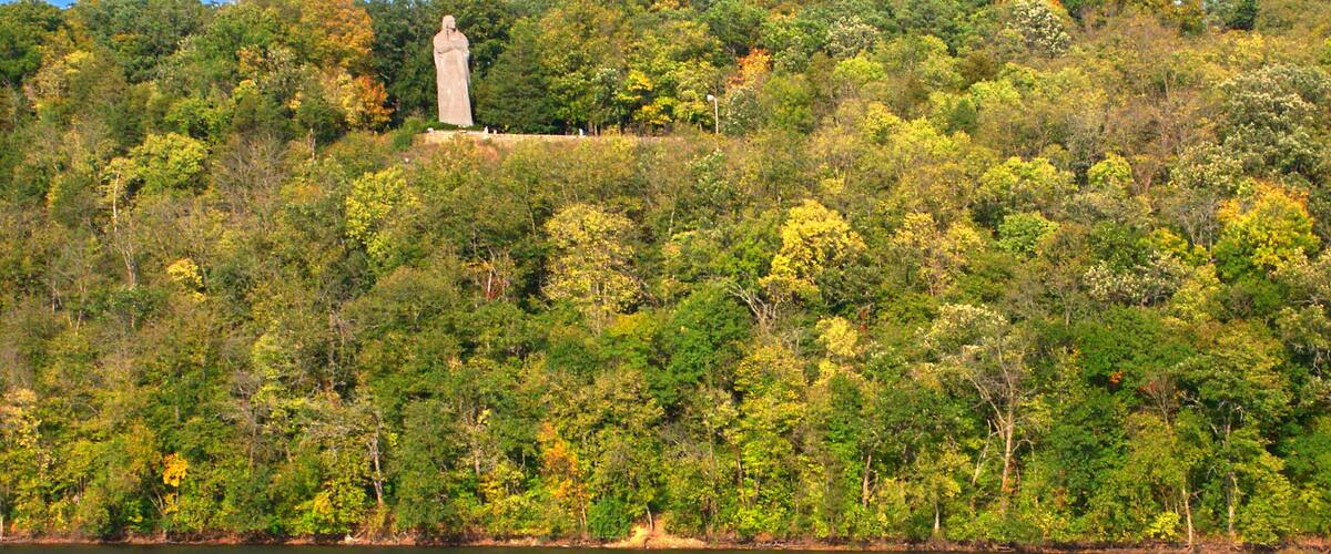 A statue on a hill with a lake in the foreground.