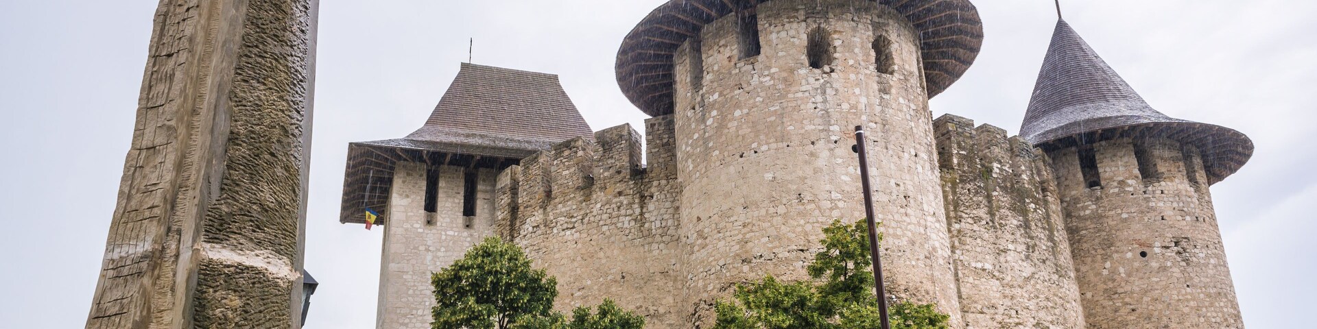 Um castelo histórico com várias torres e um imponente obelisco de pedra em primeiro plano.