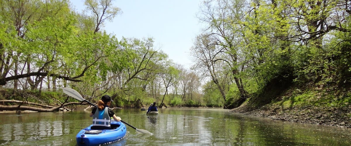 A calm river with kayaks, surrounded by lush green trees.