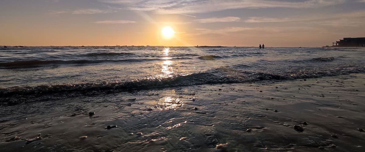 A beach at sunset with waves and a clear sky.