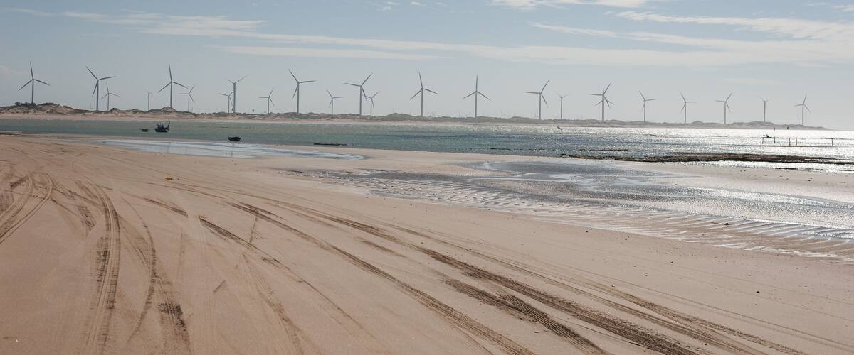 A sandy beach with tire tracks and wind turbines in the distance.