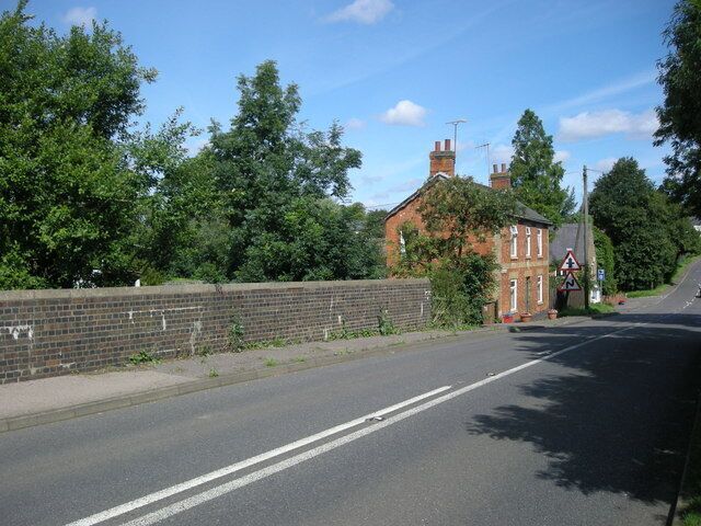 A quiet road with a brick wall on one side and a house with a red roof in the distance.