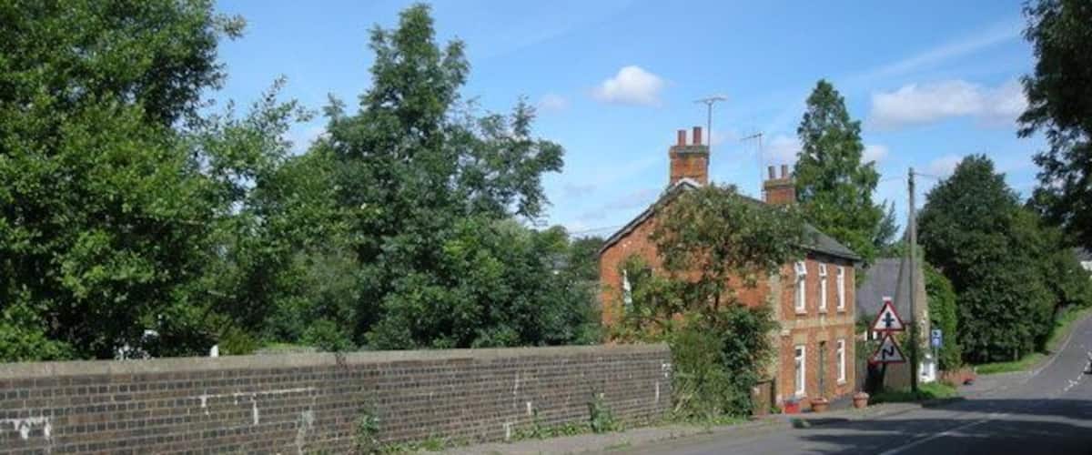A quiet road with a brick wall on one side and a house with a red roof in the distance.
