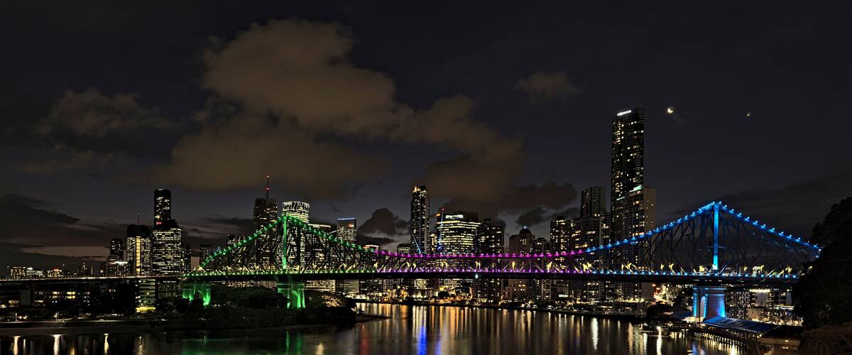 A city skyline at night with illuminated skyscrapers and a bridge with colorful lights.