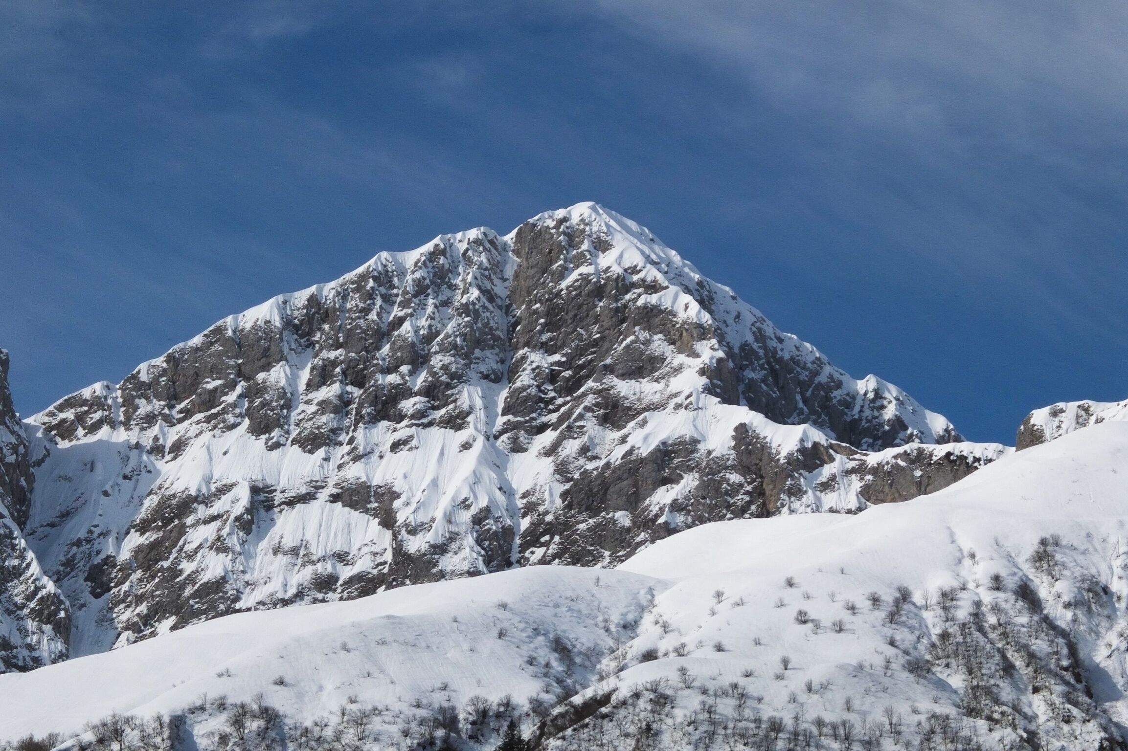 A snow-covered mountain peak with rugged terrain and a clear blue sky.