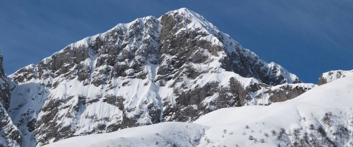 A snow-covered mountain peak with rugged terrain and a clear blue sky.