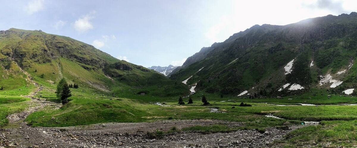 A mountainous landscape with a river flowing through a valley, surrounded by green hills and rocky outcrops.