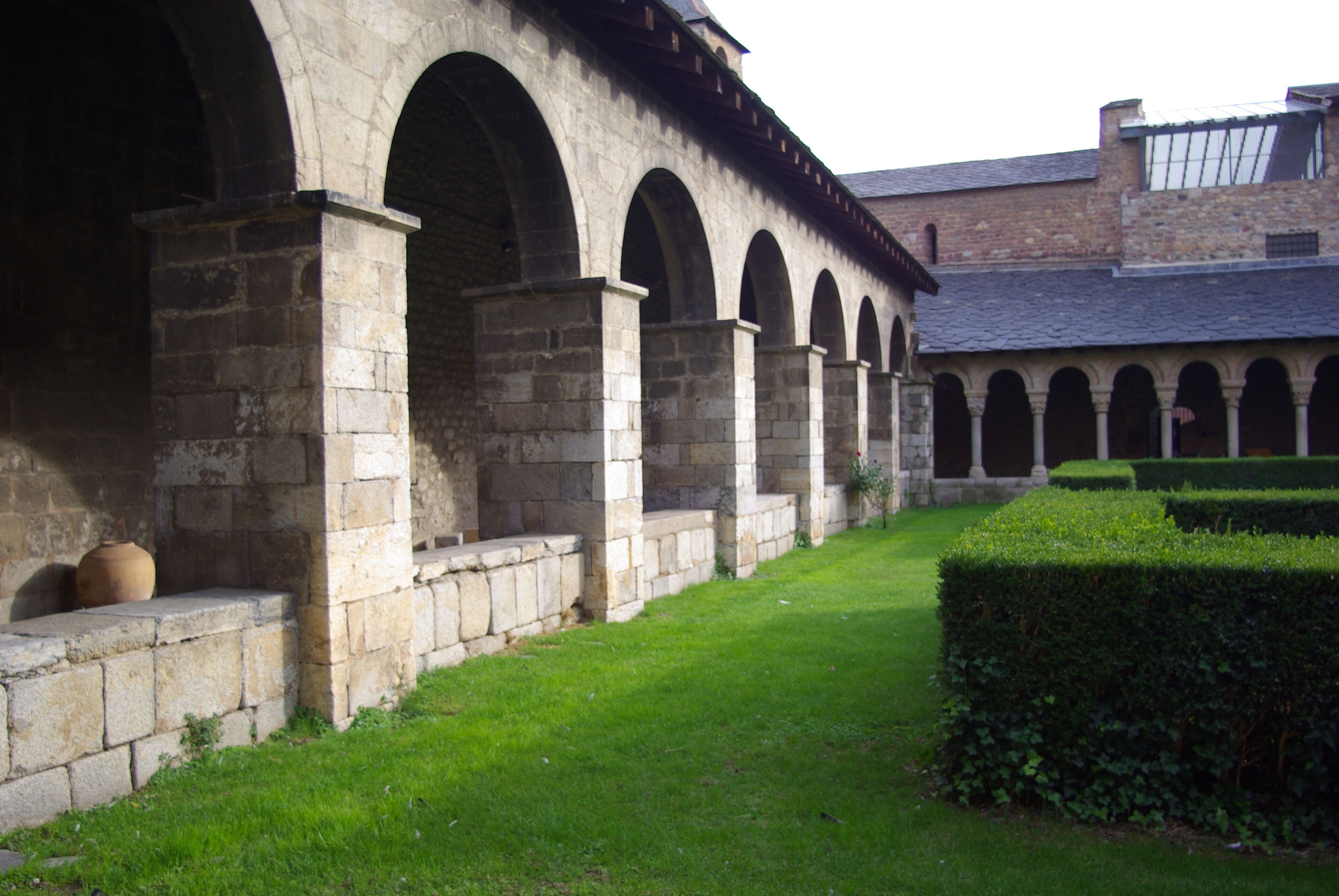A stone building with arched walkways and a well-maintained hedge.