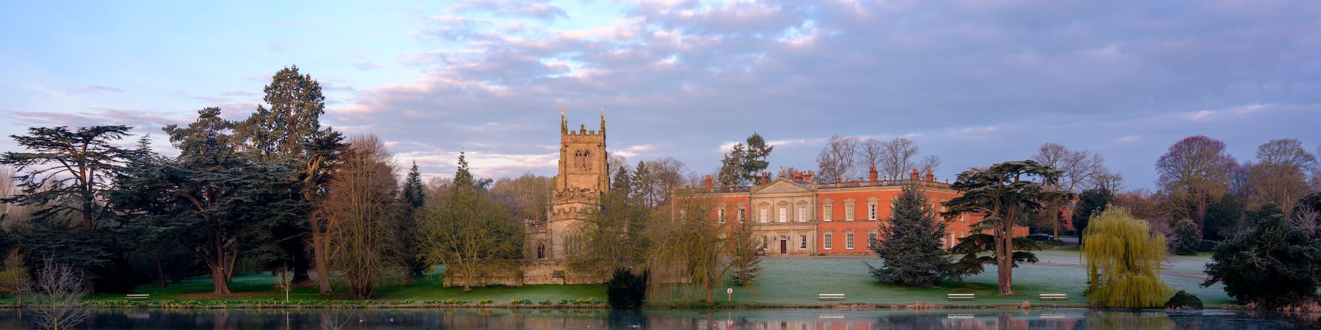A historic building with a tower, a lake, and frost-covered grass.