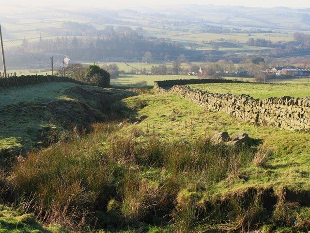 A rural landscape with stone walls, grassy fields, and distant buildings.