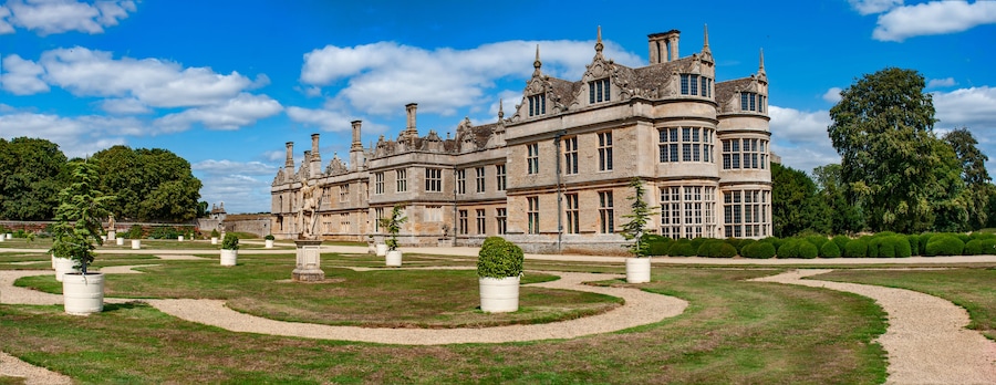 Um edifício grande e histórico com arquitetura elaborada, rodeado por jardins bem cuidados e caminhos.