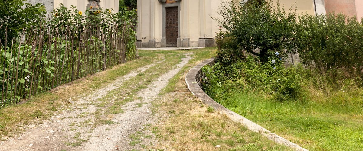 A church with a clock tower, surrounded by greenery and mountains.