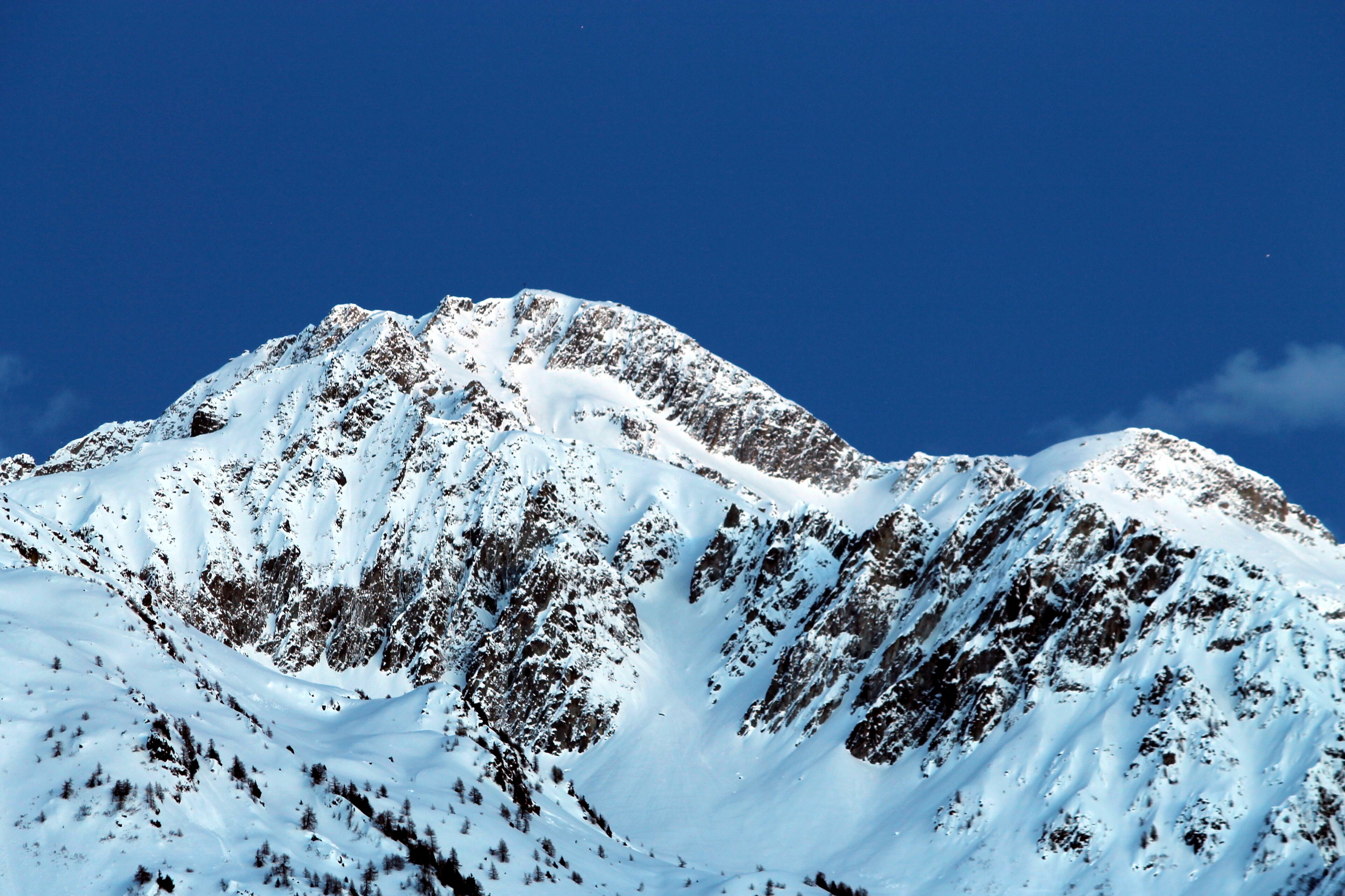 Un pico montañoso cubierto de nieve, con terreno accidentado y un cielo azul despejado.