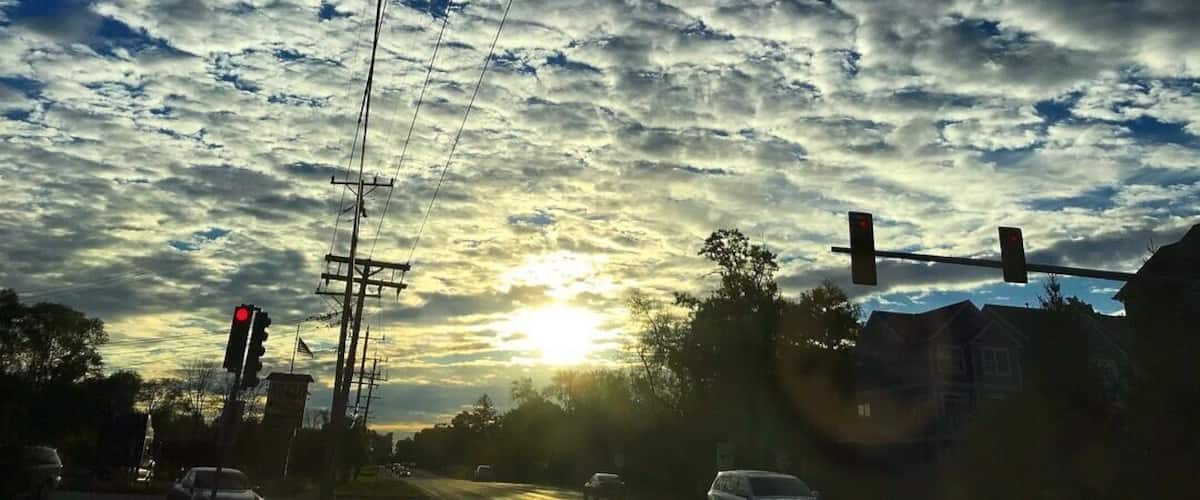 A sunset with a cloudy sky, traffic lights, and power lines.