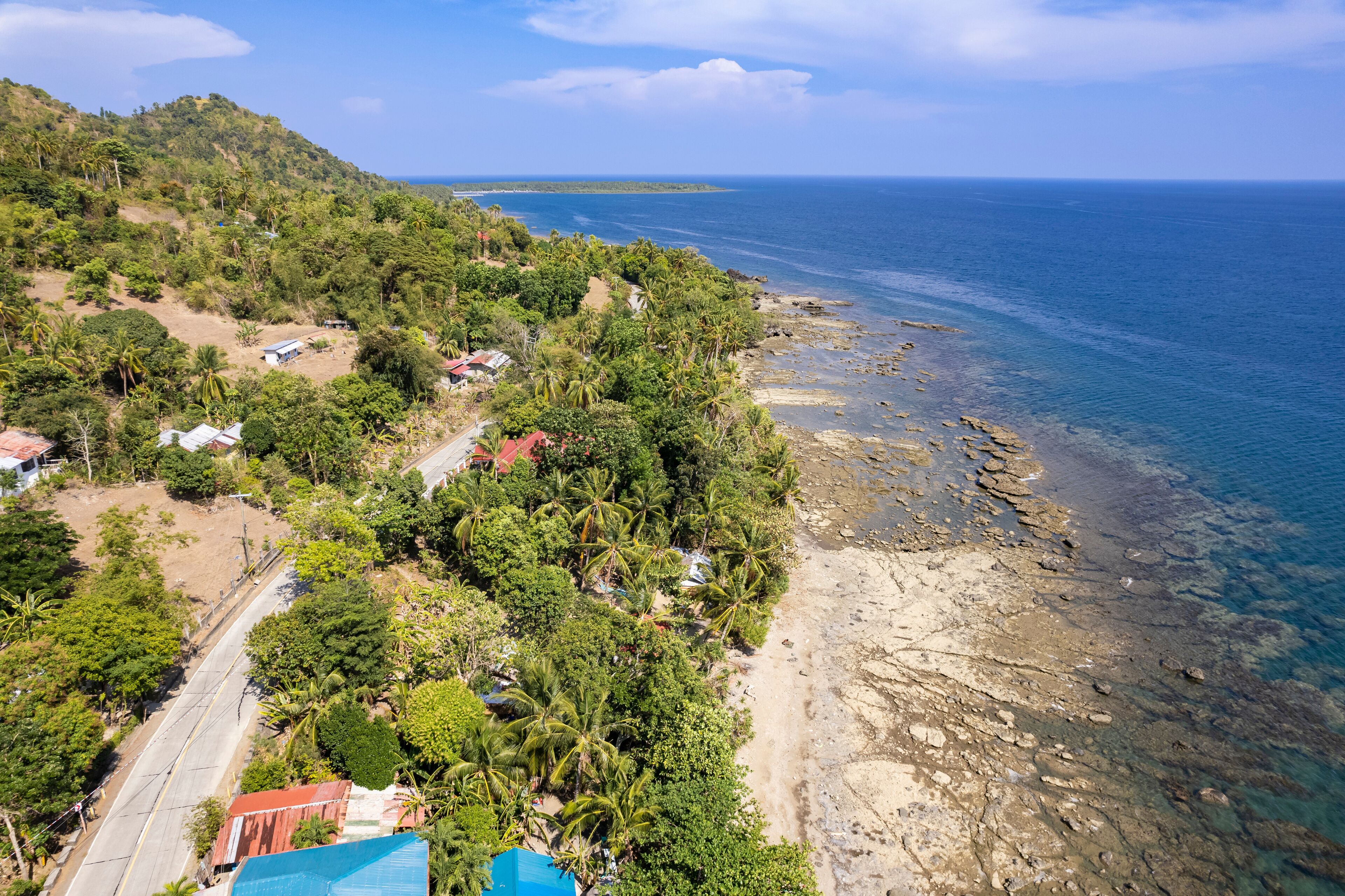 A coastal landscape with a beach, rocky shoreline, and lush greenery.