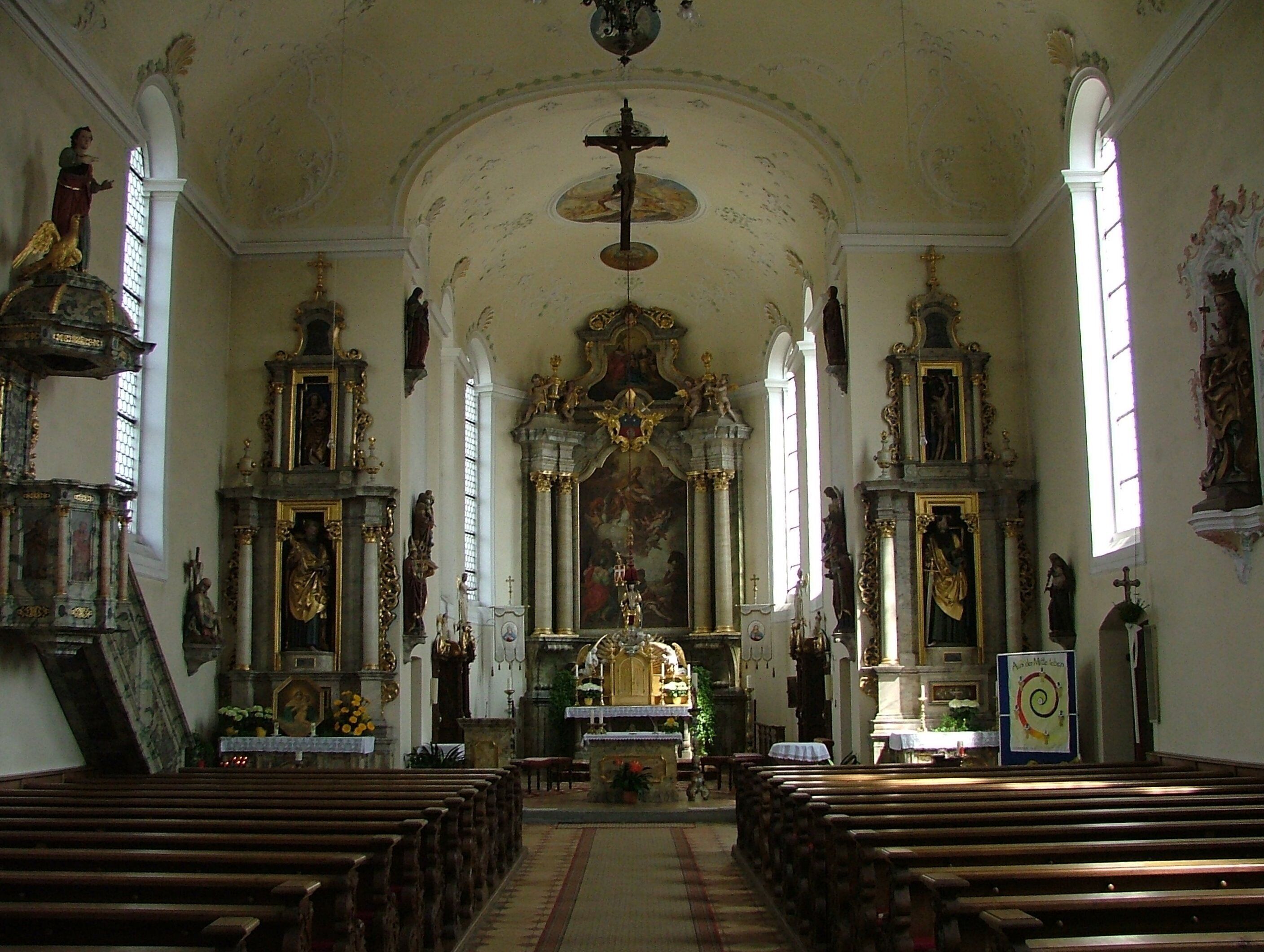An ornate church interior with wooden pews, a central altar, and religious statues.