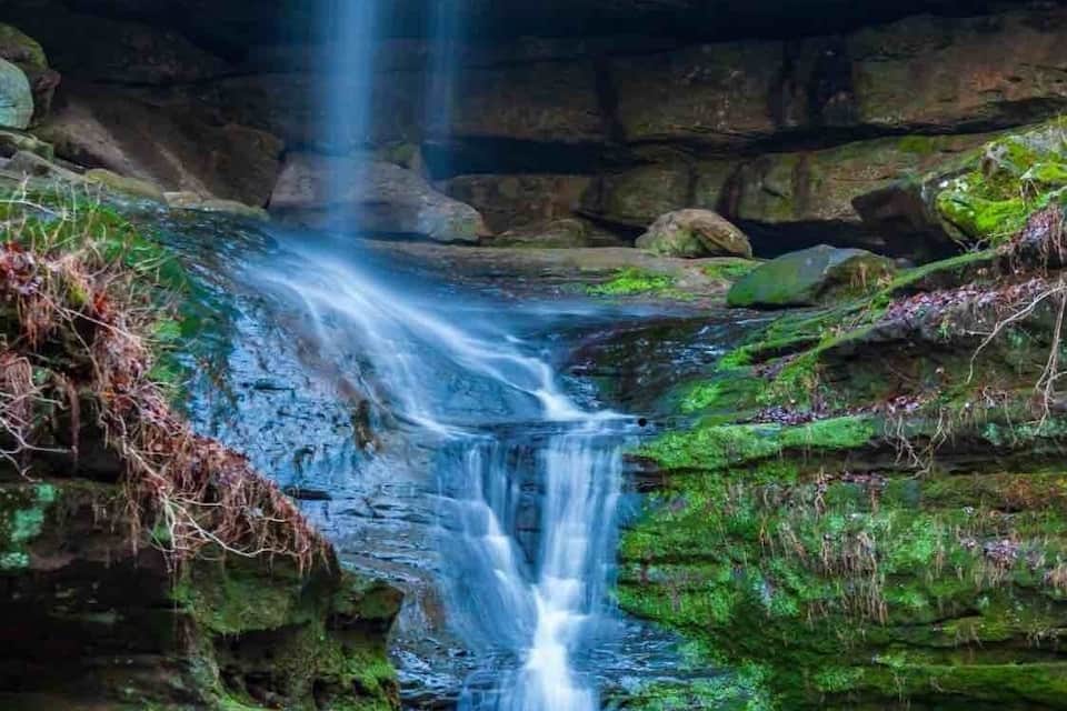 A waterfall cascading down a rocky cliff surrounded by lush greenery.