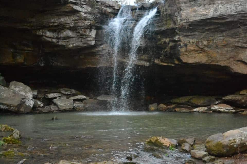 A waterfall cascading into a clear pool surrounded by rocky terrain and trees.