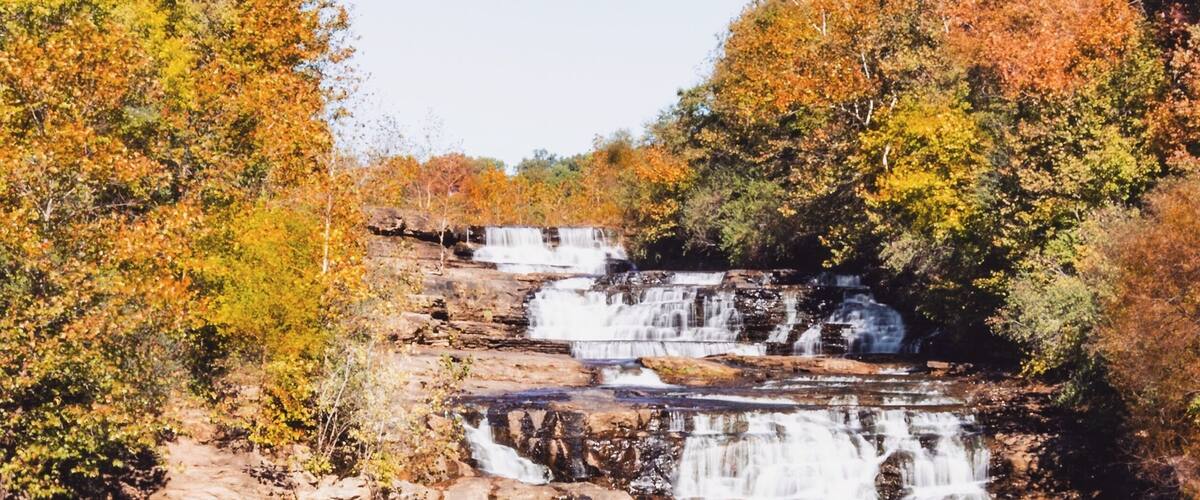 A waterfall cascading over rocky terrain surrounded by autumn-colored trees.