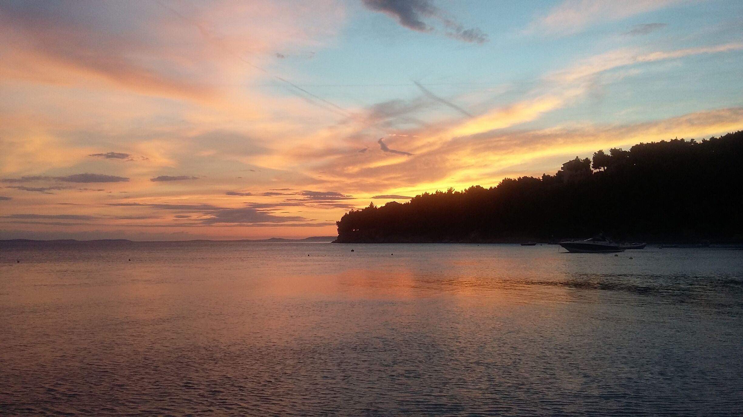 A sunset over a calm sea with a forested coastline.