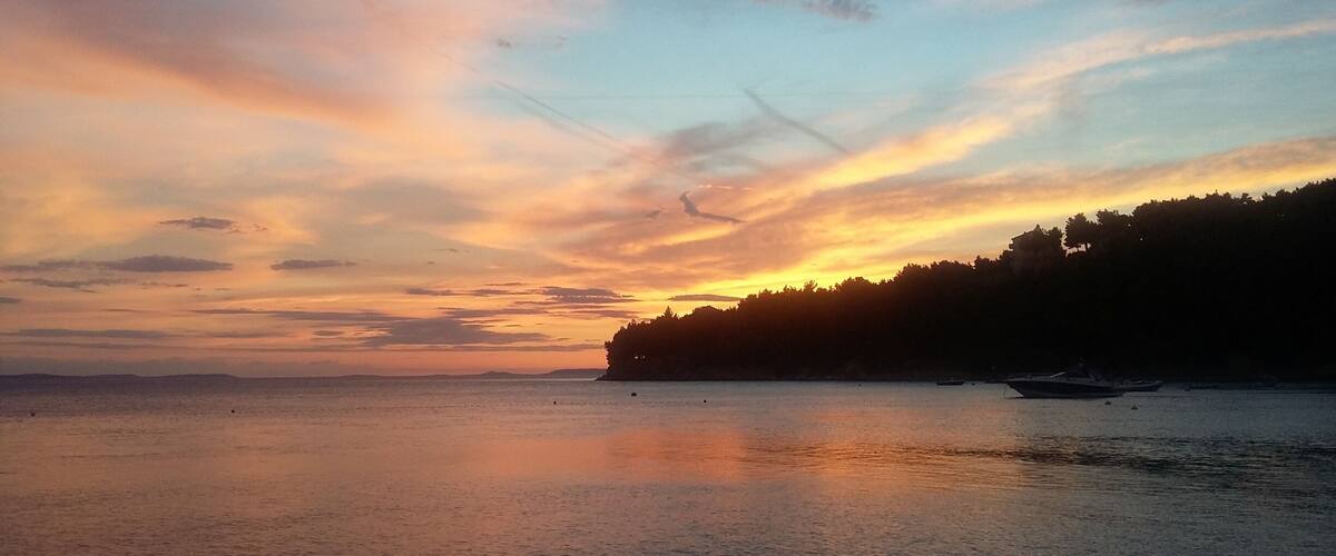 A sunset over a calm sea with a forested coastline.